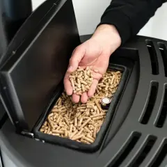 Dłoń wsypuje pellet do zasobnika pieca. Szukasz alternatywy co zamiast pelletu?