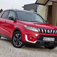 Czerwony Suzuki Vitara Hybrid z czarnym dachem, zaparkowany na żwirowej nawierzchni.