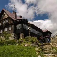 Schody prowadzą do drewnianego schroniska w górach izerskich Polska. W tle błękitne niebo z chmurami.