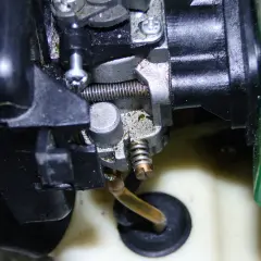Zbliżenie na gaźnik do kosy spalinowej, widoczne elementy metalowe i plastikowe, przewód paliwowy.