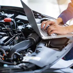 Mechanik diagnozuje brak mocy na ciepłym silniku benzyna, używając laptopa do analizy danych z jednostki napędowej.