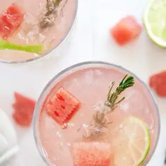 Två glas med en rosa, alkoholfri drink med is, vattenmelonbitar, lime och rosmarin. Perfekt för en sommardag.