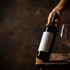 Dłoń trzyma butelkę wina nad pustym kieliszkiem, zastanawiając się, czy wino zamarza.