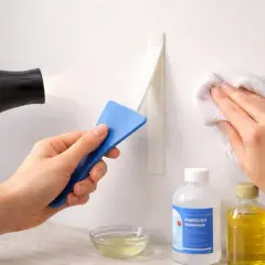 Comment enlever des traces de scotch : un sèche-cheveux chauffe un adhésif, une spatule bleue le décolle, et un chiffon blanc nettoie le mur.