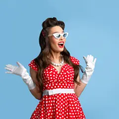 Kobieta w stylu pin-up w czerwonej sukience w grochy, białych rękawiczkach i okularach, z szeroko otwartymi ustami i rękami uniesionymi w geście zaskoczenia.