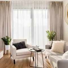 Przytulny salon w stylu minimalistycznym. Jasna kanapa, fotel, stolik kawowy i telewizor tworzą harmonijną przestrzeń.