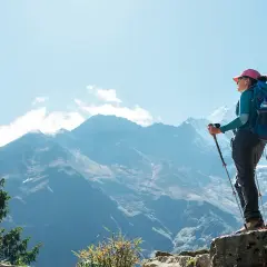 Kobieta z plecakiem i kijkami trekkingowymi podziwia majestatyczne góry. To jej wycieczka na Mount Everest, pełna wyzwań i piękna.