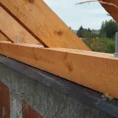Drewniana murłata z widocznymi wymiarami, przykręcona do betonowego wieńca. W tle drzewa i domy.