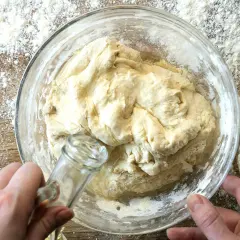Dłoń dodaje olej do ciasta na roti w szklanej misce, otoczonej mąką.