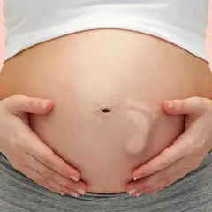 Brzuszek w 29 tygodniu ciąży, z widocznym odciskiem stópki dziecka. Ręce delikatnie obejmują brzuch.