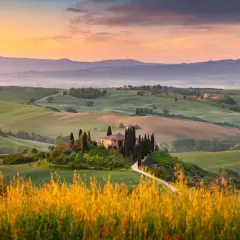 Dolci colline verdi nel Val d'Orcia, con una casa colonica e cipressi su una collina, al tramonto.