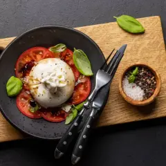 Pyszny **burrata przepis** na talerzu z pomidorami i bazylią. Obok miseczka z solą i pieprzem.