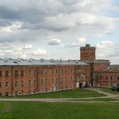 Dawny fort wojskowy w okolicach Warszawy, z ceglanymi budynkami i wieżą.