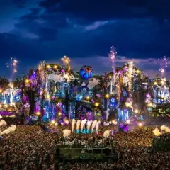 Un'enorme folla attende l'inizio del line up Tomorrowland, illuminata da fuochi d'artificio e luci psichedeliche su un palco fantastico.