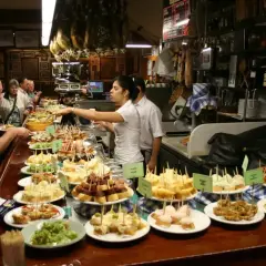 Bar pełen różnorodnych tapas, czyli małych przekąsek. Ludzie wybierają swoje ulubione smaki.