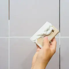 Dłoń z kielnią nakłada fugę na fugę, odnawiając fugi między płytkami.
