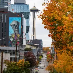 Seattle street photography captures a vibrant autumn scene with colorful trees, a mural, and the Space Needle in the distance.