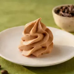 Kremowy mus kawowy z mascarpone na białym talerzyku, obok ziarna kawy.