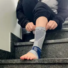 Person zieht eine Bandage am Fuß an, die bei einem Achillessehnenriss Schuh-Schmerzen helfen soll.