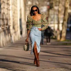 Mujer con top de cuadros y falda vaquera larga con abertura, botas altas y bolso.