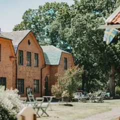 Vacker tegelbyggnad med texten "A-B. FORSVIKS BRUK". Utomhusbord och stolar inbjuder till avkoppling vid detta charmiga forsviks vandrarhem.