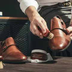 Mężczyzna czyści brązowe skórzane buty, używając szczoteczki i pasty. Dowiedz się, czym wyczyścić skórzane buty, by wyglądały jak nowe.