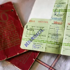 Czerwona książeczka mieszkaniowa PKO i zielone odcinki wpłat z kwotami i podpisami pracowników.