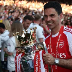 Trener Arsenalu, Mikel Arteta, z dumą trzyma puchar Premier League. Tłum kibiców świętuje sukces.