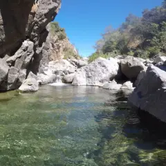 Agua cristalina en la charca de las nutrias, rodeada de rocas y vegetación bajo un cielo azul.
