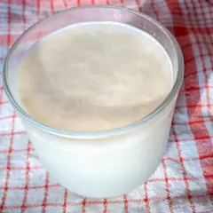 Szklanka z kremowym napojem, który może być kefir czy maślanka, stoi na czerwono-białym ręczniku.