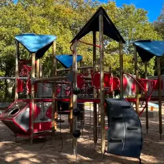 Ein bunter Spielplatz mit Klettergerüst und Schaukeln in einem der Wuppertal Parks, umgeben von Bäumen im Herbstlicht.