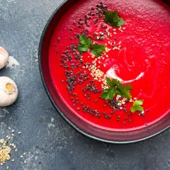 Eine leuchtend rote Bete Suppe, garniert mit Sesam und Petersilie, neben zwei Knoblauchzehen.