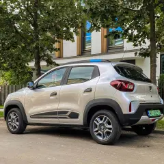 Srebrna Dacia Spring zaparkowana pod drzewami. Ten elektryczny samochód oferuje dobry zasięg na miejskie podróże.