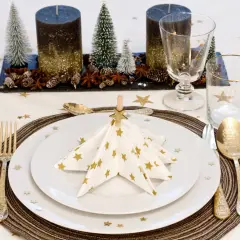 Vackert dukat bord med julgranformade servetter, stjärnmönstrat tyg och gyllene bestick.