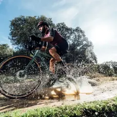 Ciclista en bici de gravel salpicando agua en un camino rural. ¡Así es el gravel!