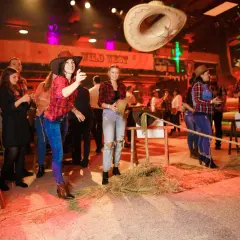 Dziewczyny w kapeluszach i kratkach bawią się na imprezie w stylu country. Rzucają kapeluszem, a w tle widać napis "Wild West".