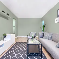 Quel mur peindre pour agrandir une pièce étroite ? Ce salon moderne aux murs vert pâle, avec un canapé gris et des cadres photos, offre une ambiance apaisante.