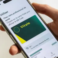 Main d'une personne tenant un smartphone affichant la carte Vitale numérique. Idéal pour le courrier restitution carte vitale.