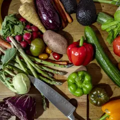 Buntes Arrangement von frischem Gemüse und Obst, darunter Bananen, Paprika, Tomaten, Gurken, Auberginen und Spargel. Ein Messer liegt daneben. Alles für gesundes Essen.