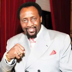Thomas Hearns now, a boxing legend, smiles confidently in a light grey suit, red tie, and pocket square.