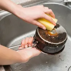 Nettoyage d'une casserole brûlée avec une éponge. Le bicarbonate de soude sera utile pour cette tâche difficile.