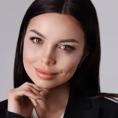 Elegancka kobieta w czarnej marynarce, opierająca podbródek na dłoni, pozuje w studiu.