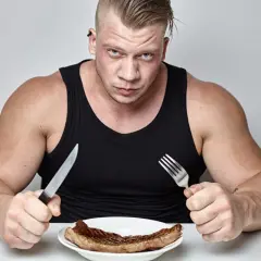 Mężczyzna z widoczną muskulaturą, gotowy do jedzenia steka. Chcesz wiedzieć, jak przytyć? Zacznij od solidnego posiłku!
