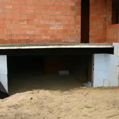 Budowa piwnicy: widok fundamentów i ścian z pustaków. Piasek wokół, widać izolację.