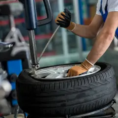 Mechanik w niebieskim kombinezonie wykonuje wymianę opon z czujnikami ciśnienia, używając narzędzi do demontażu.