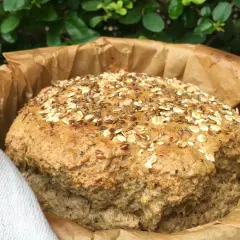 Pan de lino recién horneado, cubierto de semillas y avena, envuelto en papel de hornear.