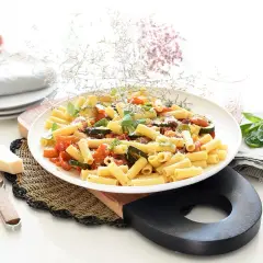 Plato de pasta con verduras salteadas, calabacín, tomate y albahaca, con queso parmesano rallado.