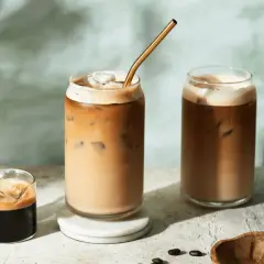 Deux verres de latte froid avec une paille dorée, un petit shot d'espresso et des grains de café.