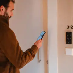 Hombre con móvil frente a puerta con teclado numérico. Una de las desventajas de la domótica es la dependencia tecnológica.