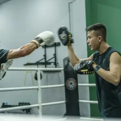 Two boxers train in a ring, one throwing a punch at the other's mitts during a reflex bag workout.